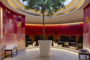 A lobby with a large tree, seating area, and a red wall with abstract art. - Cresta Palace (Celerina-Schlarigna)
