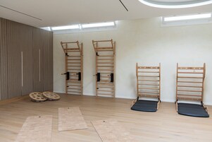 Una habitación con techo inclinado, suelo de madera y tres equipos de ejercicio fijados a la pared.