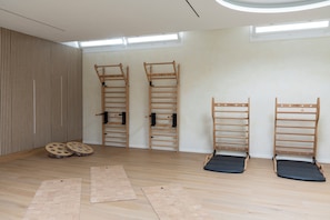 Una habitación con techo inclinado, suelo de madera y tres equipos de ejercicio fijados a la pared.