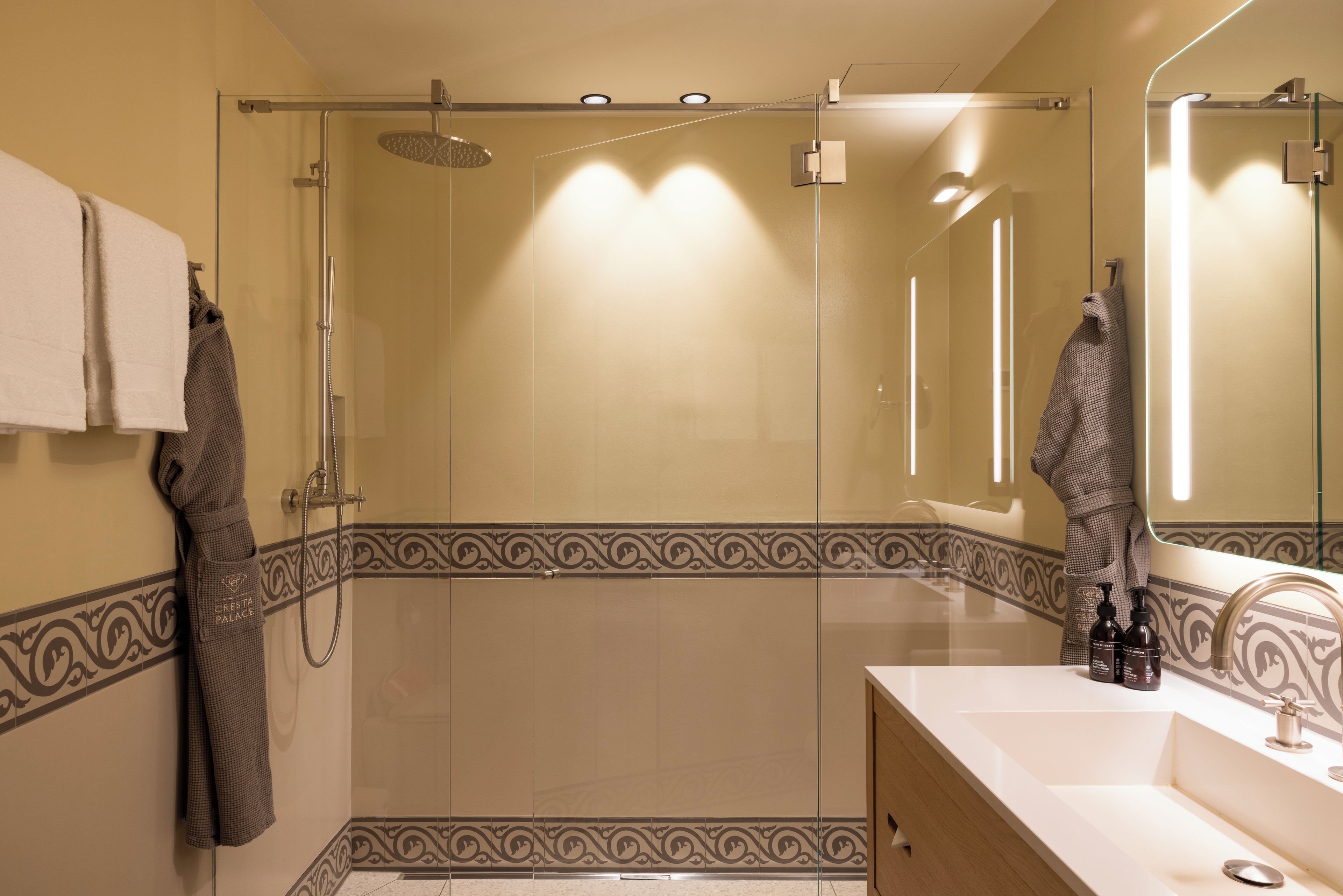 A modern bathroom with a glass-enclosed shower, a vanity with a mirror, and decorative wall tiles.