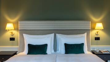 Habitación de hotel con una cama grande, dos lámparas de noche y una mesita de noche con un vaso de agua y un libro.