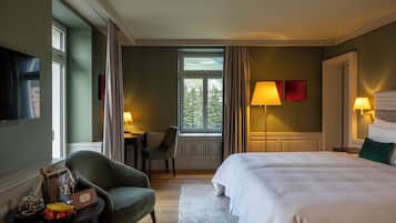 Una habitación de hotel con cama, escritorio, silla, televisor y ventana con cortinas.