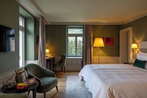 A hotel room with a bed, a desk, a chair, a TV, and a window with curtains. - Cresta Palace (Celerina-Schlarigna)