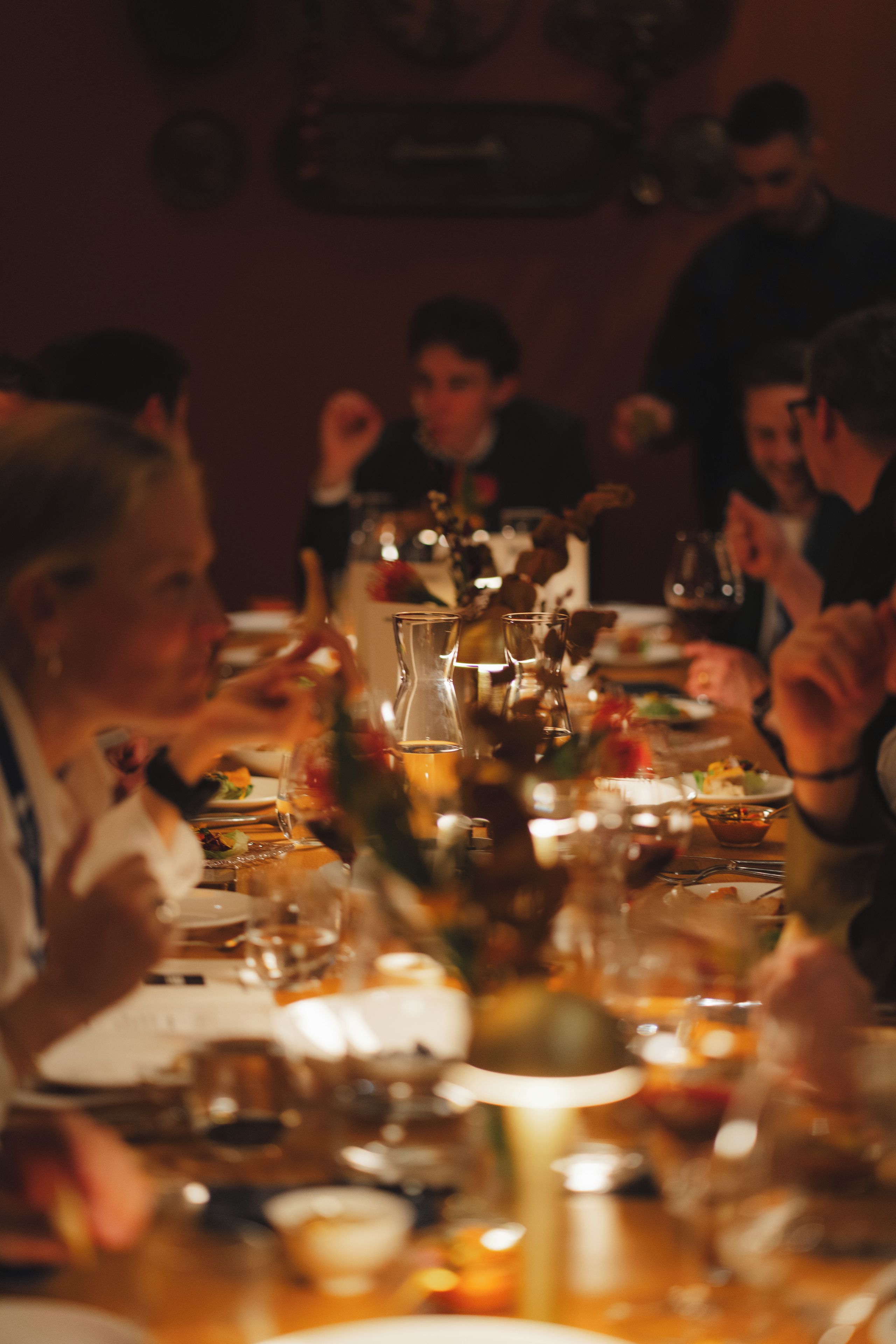 Une table à manger, dressée avec différents plats et verres, autour de laquelle sont rassemblées des personnes.
