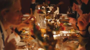 Une table à manger, dressée avec différents plats et verres, autour de laquelle sont rassemblées des personnes.