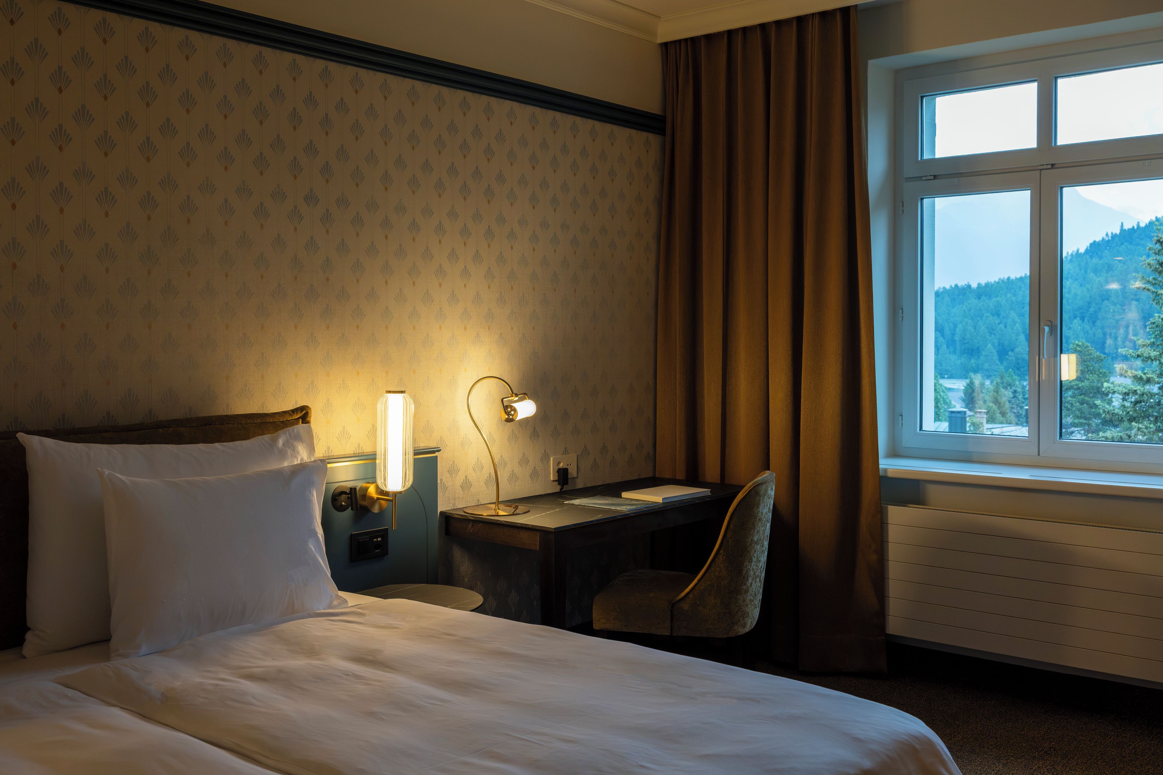 Habitación de hotel con cama, escritorio, silla y ventana con vistas a un área boscosa.