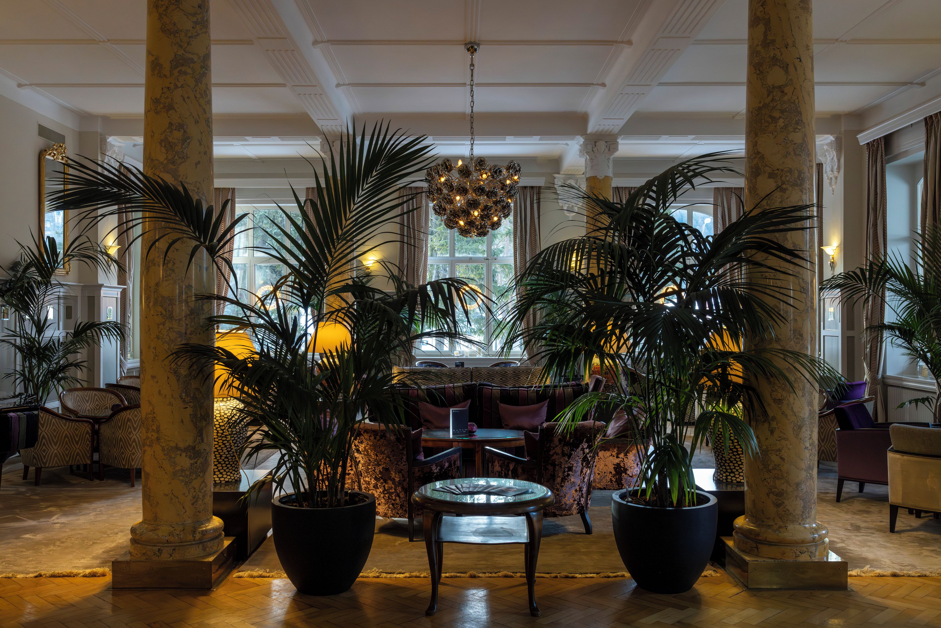 A lobby with a central seating area, large potted plants, and a chandelier.
