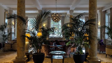 A lobby with a central seating area, large potted plants, and a chandelier.