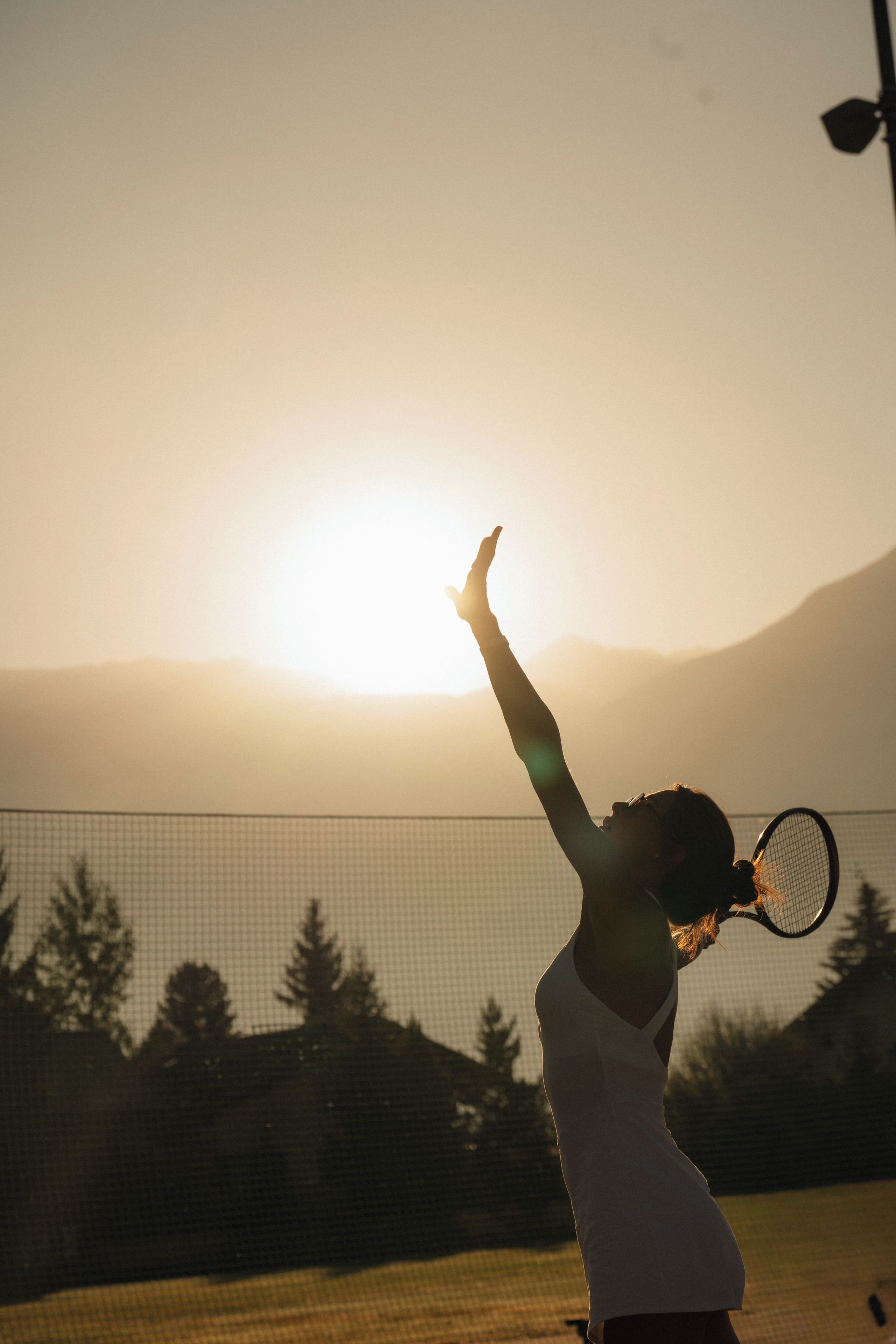 Eine Tennisspielerin in einem weißen Tanktop mit Tennisracket hebt ihren Arm in Siegestrahl.