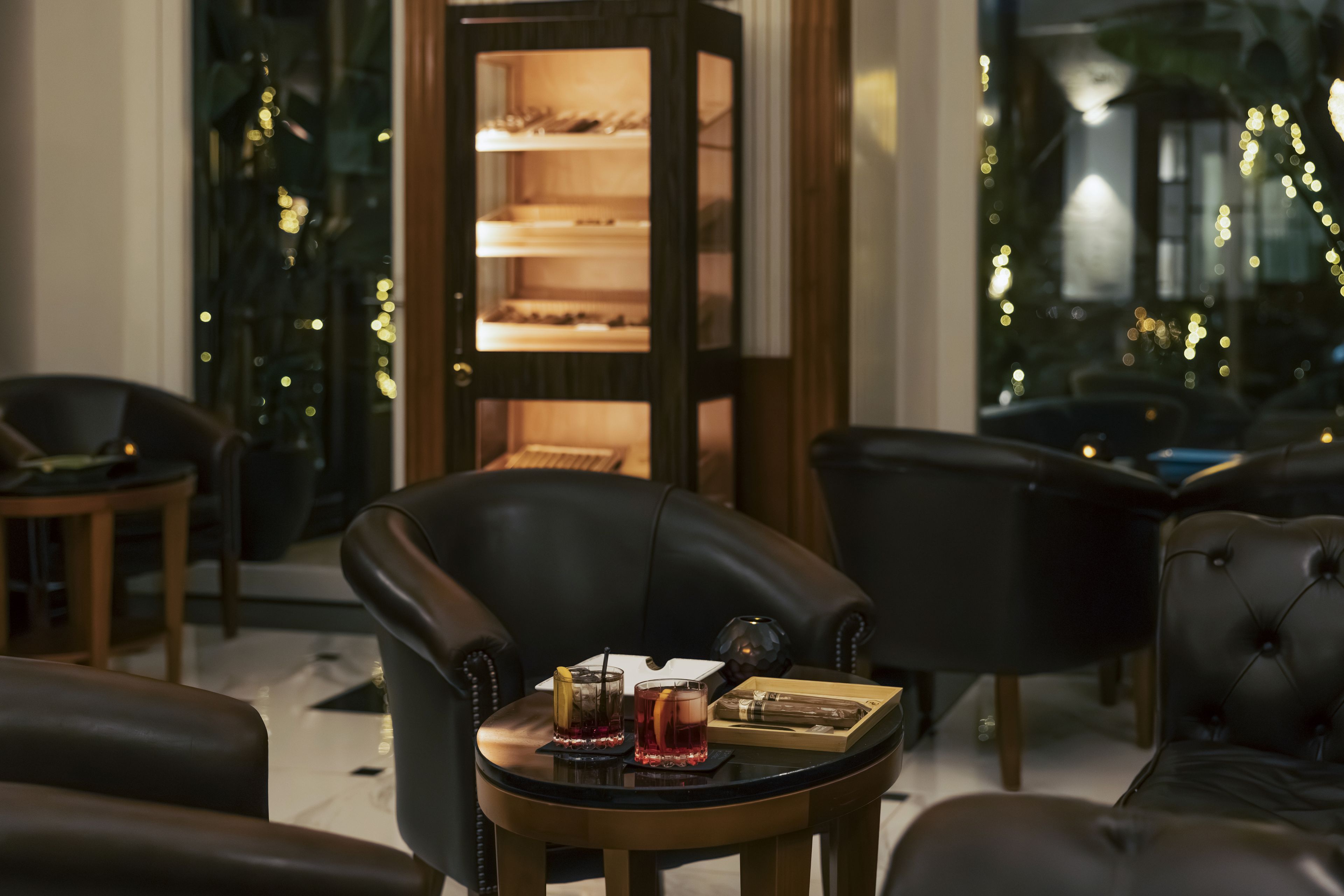 A modern interior with leather armchairs, a small round table with drinks, and a decorative cabinet with shelves.