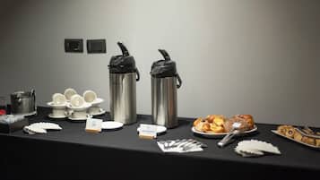 A buffet table with coffee pots, teapots, cups, plates of pastries, and utensils.
