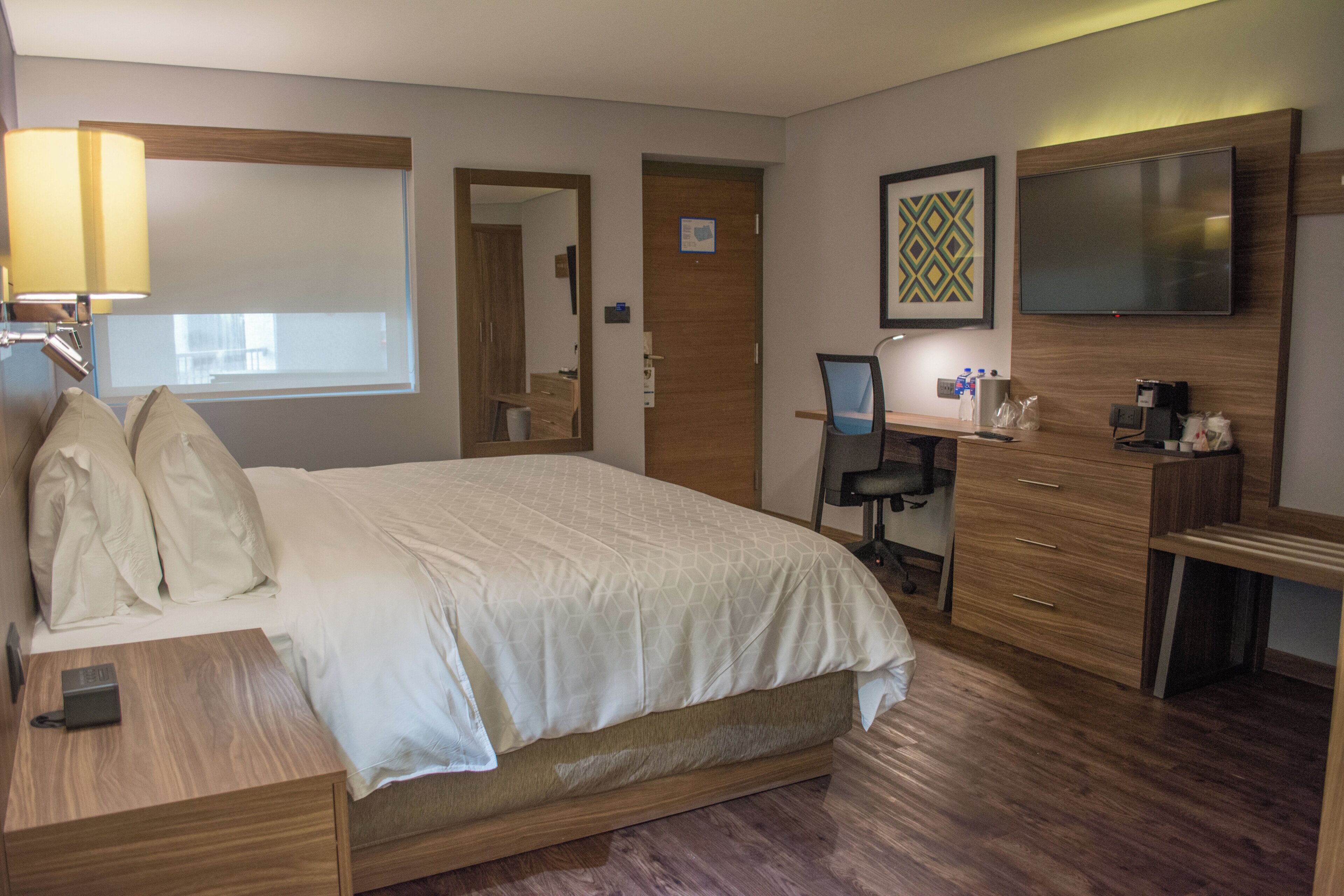 A hotel room with a bed, a desk, a chair, a television, and a mirror.