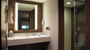 A modern bathroom with a large mirror, a sink with soap dispensers, a towel rack, and a glass-enclosed shower.