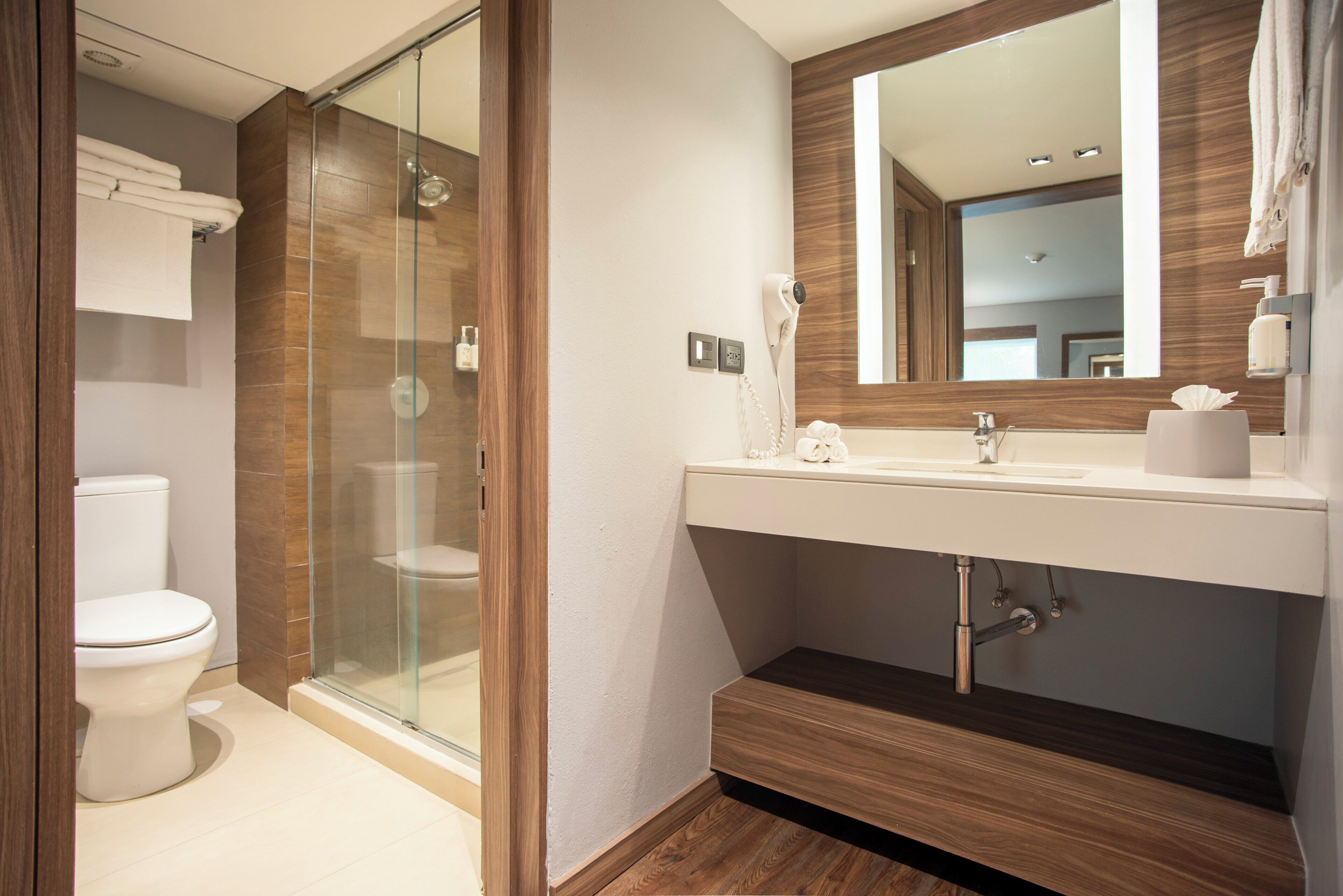 A modern bathroom with a glass-enclosed shower, a white toilet, and a vanity with a mirror and towel rack.