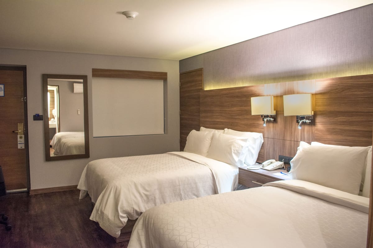 Une chambre d’hôtel avec deux lits, une table de chevet avec un téléphone, un miroir et des lampes fixées au mur.