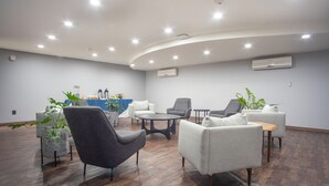 Un área de estar moderna con techo curvo, iluminación empotrada y una combinación de sillas tapizadas en gris y blanco.