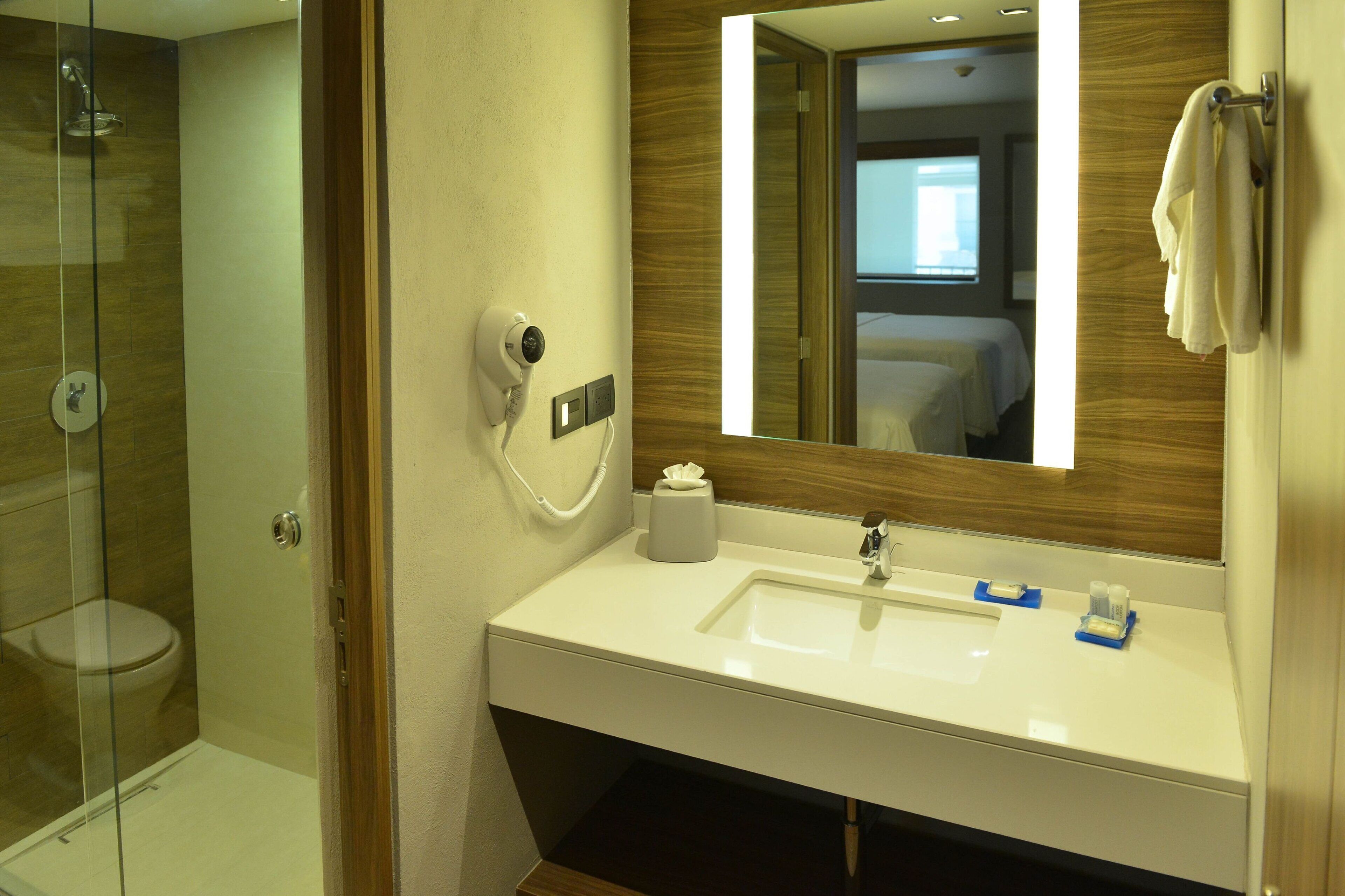 Ein Hotelbadezimmer mit Duschkabine aus Glas, einem weißen Waschbecken mit Spiegel und einem Handtuchhalter.