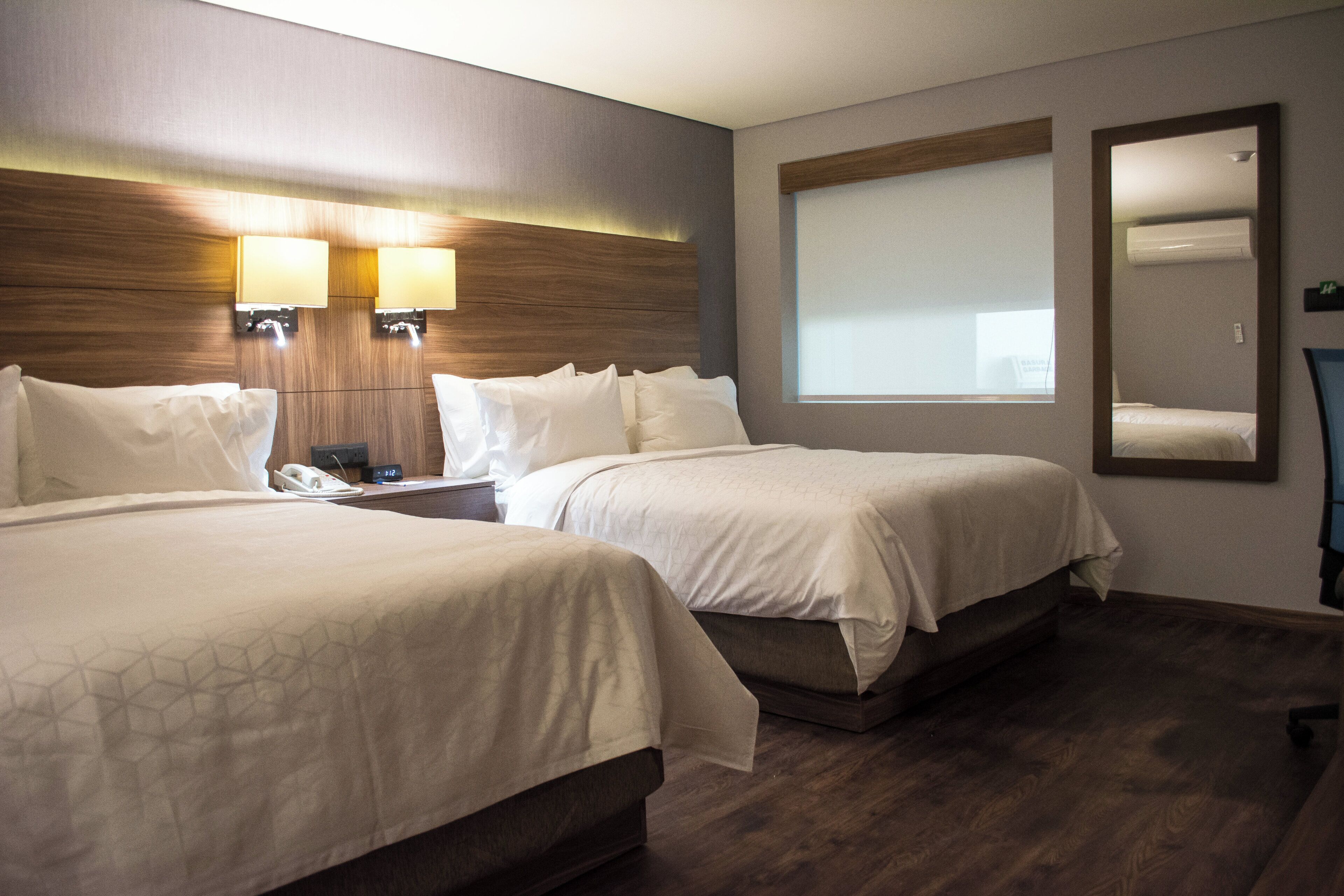Une chambre d’hôtel avec deux lits, une table de chevet avec un téléphone et une lampe fixée au mur.