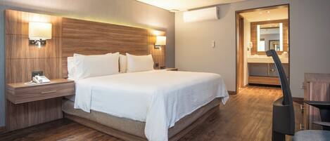 Una habitación de hotel moderna con una cama grande, cabecera de madera, lámparas de noche, una mesita de noche y un espejo.