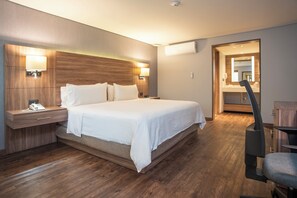 Una habitación de hotel moderna con una cama grande, cabecera de madera, lámparas de noche, una mesita de noche y un espejo.