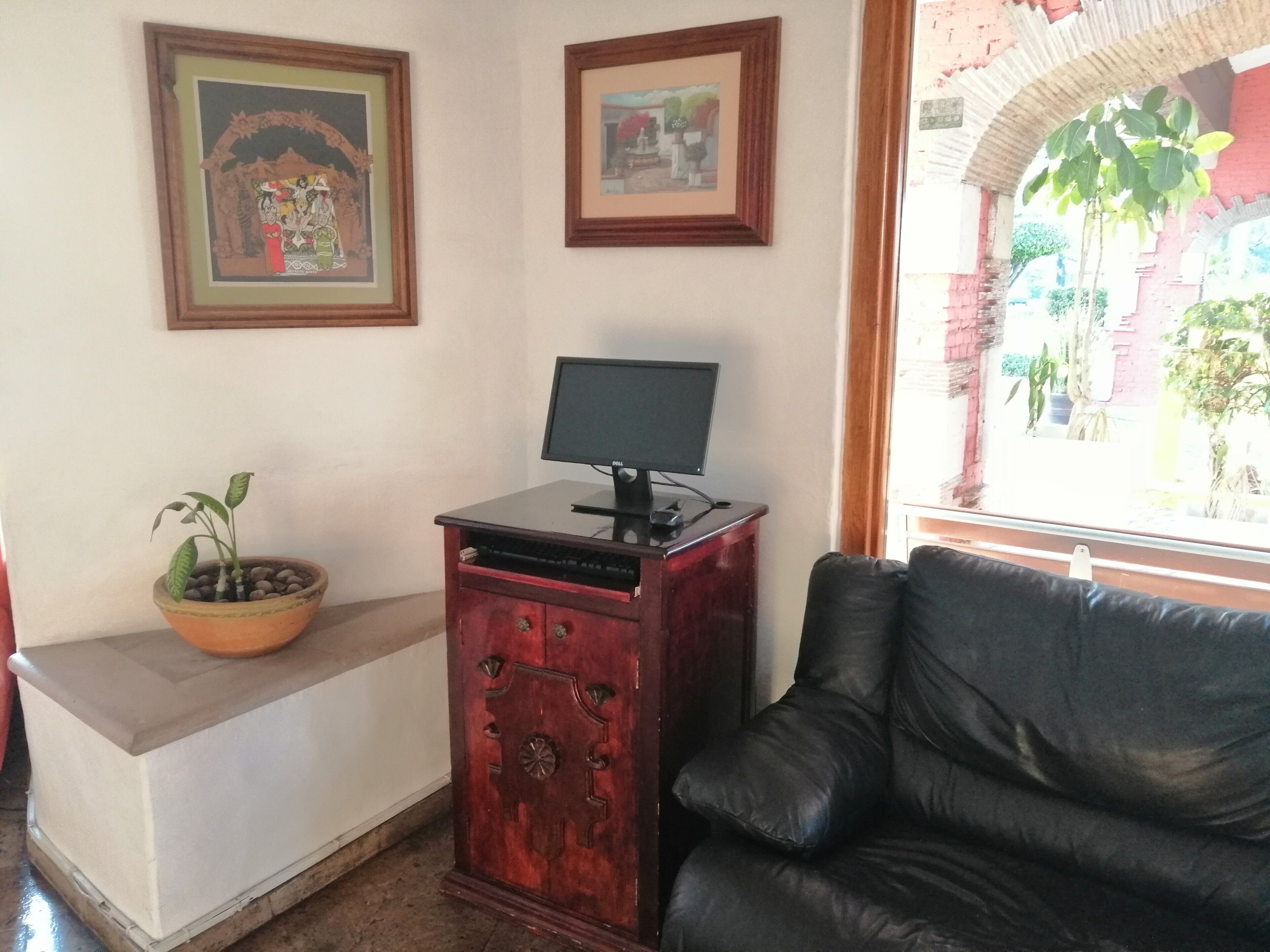 A room with a black leather sofa, a wooden cabinet with a monitor, a potted plant, and two framed pictures on the wall.