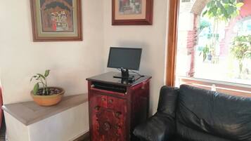 A room with a black leather sofa, a wooden cabinet with a monitor, a potted plant, and two framed pictures on the wall.