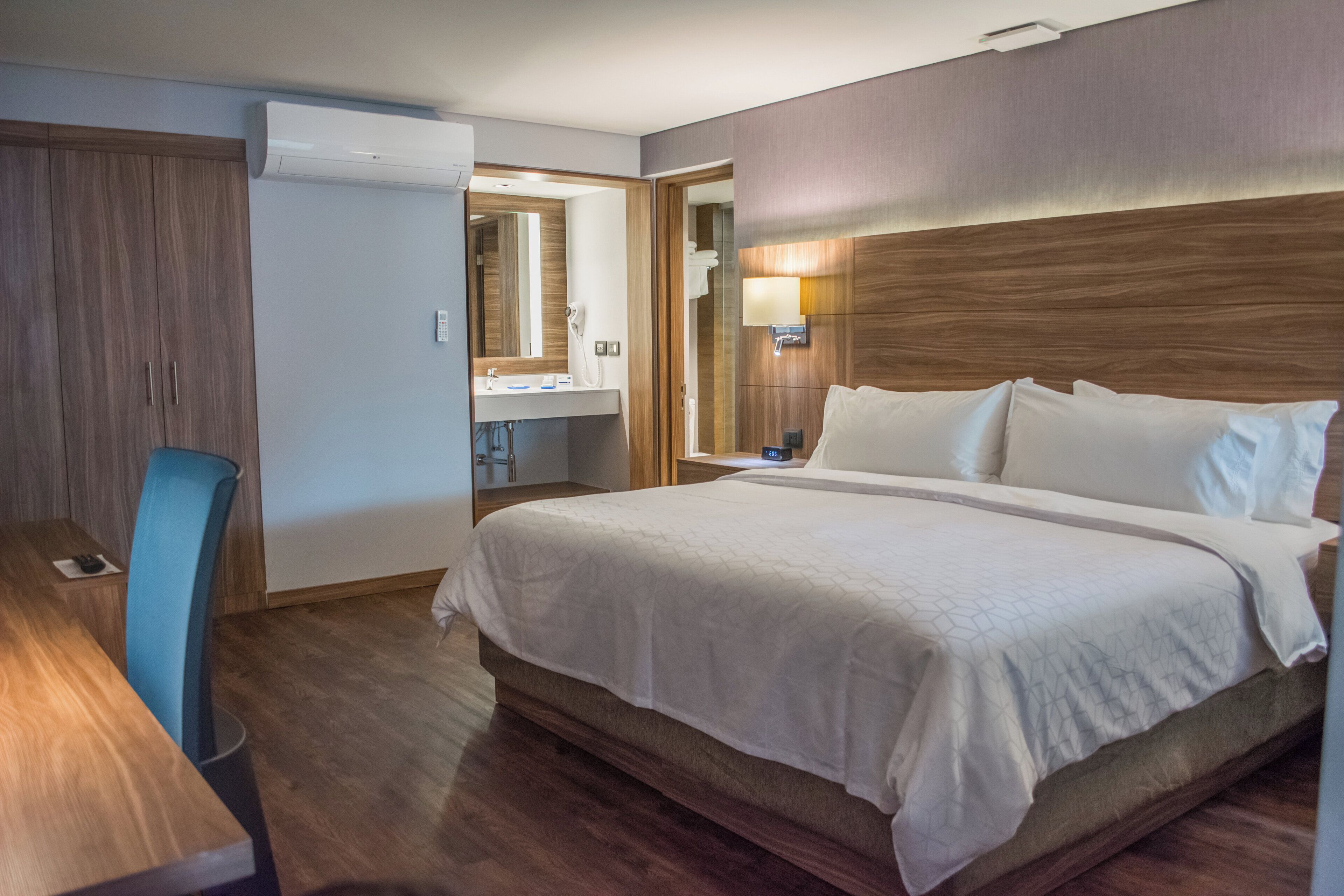 Ein Hotelzimmer mit Bett, Schreibtisch, Stuhl und einem Badezimmer mit Spiegel sowie einer Wand-Klimaanlage.