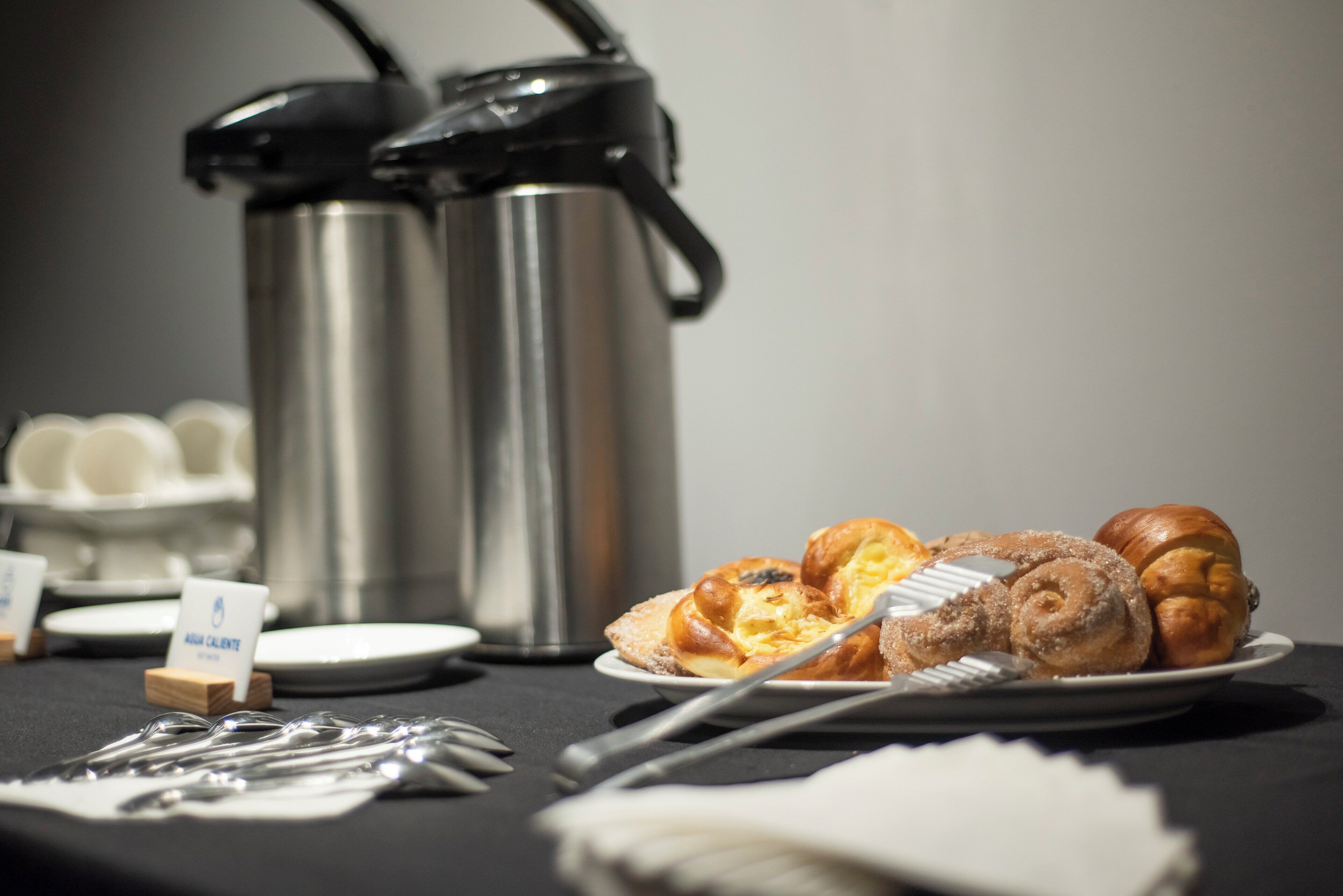 A breakfast setup with pastries, a coffee maker, and utensils on a table.