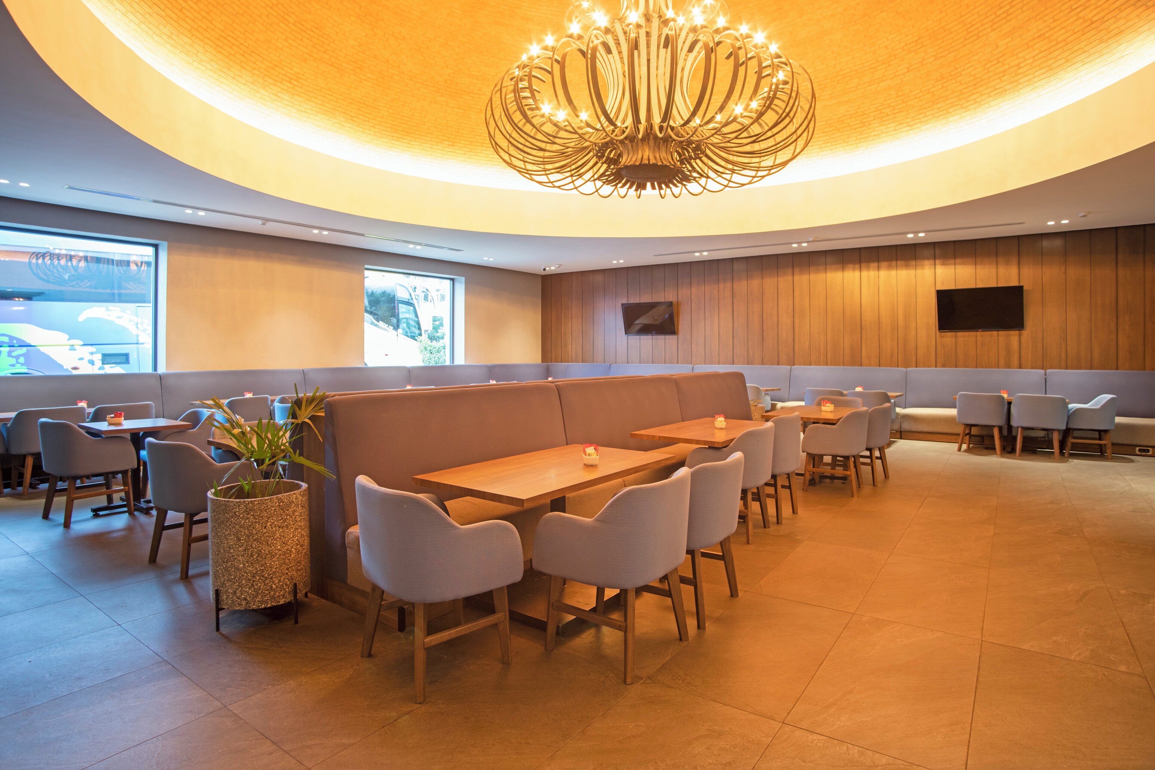 Un restaurant moderne doté d’un plafond incurvé, de murs lambrés et d’un espace central avec des tables et des chaises.