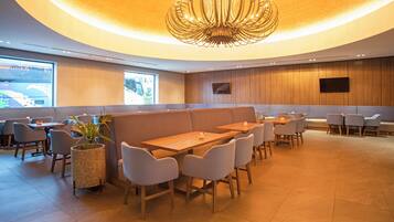 Un restaurant moderne doté d’un plafond incurvé, de murs lambrés et d’un espace central avec des tables et des chaises.
