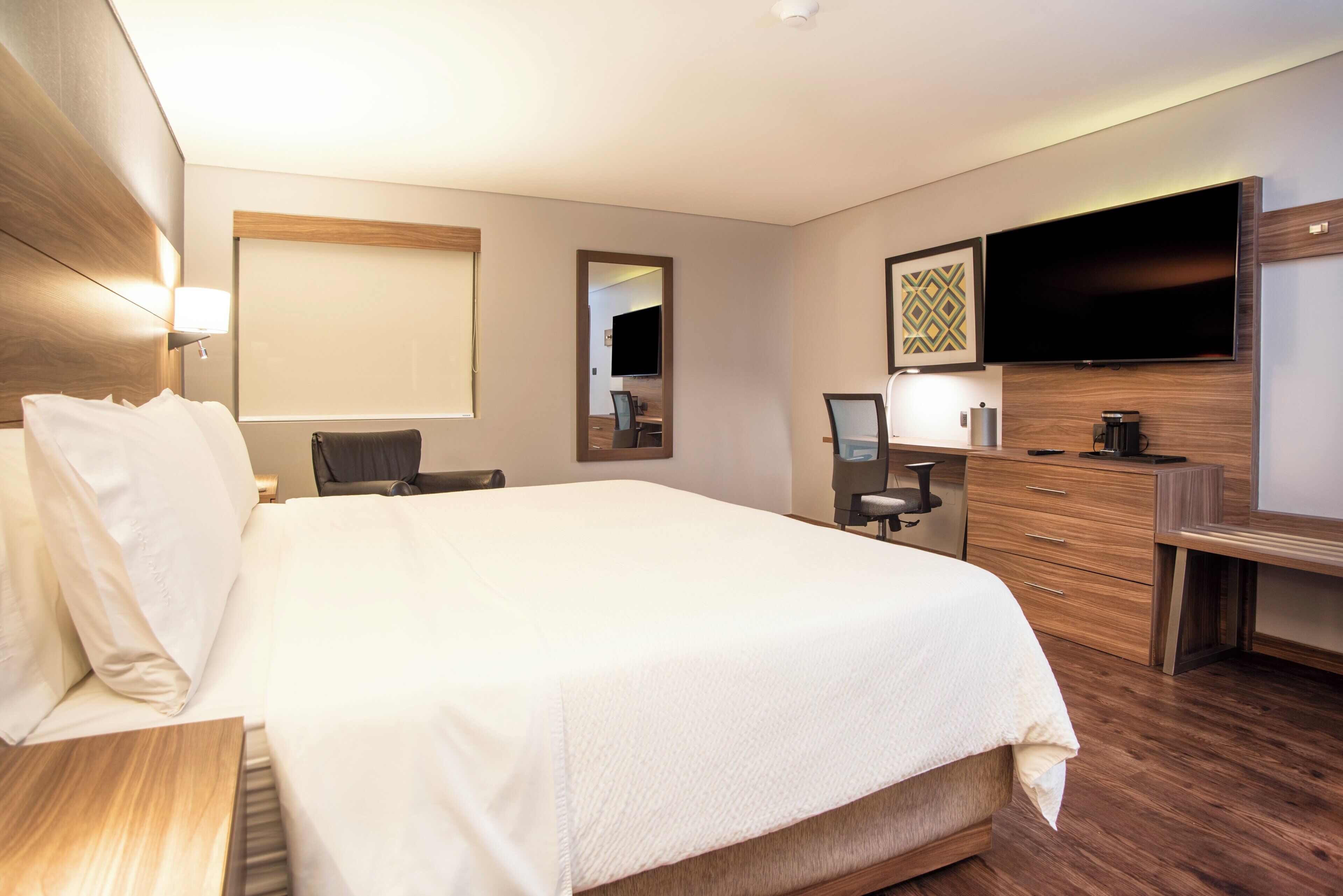 A hotel room with a large bed, a desk, a chair, a TV, and a dresser.