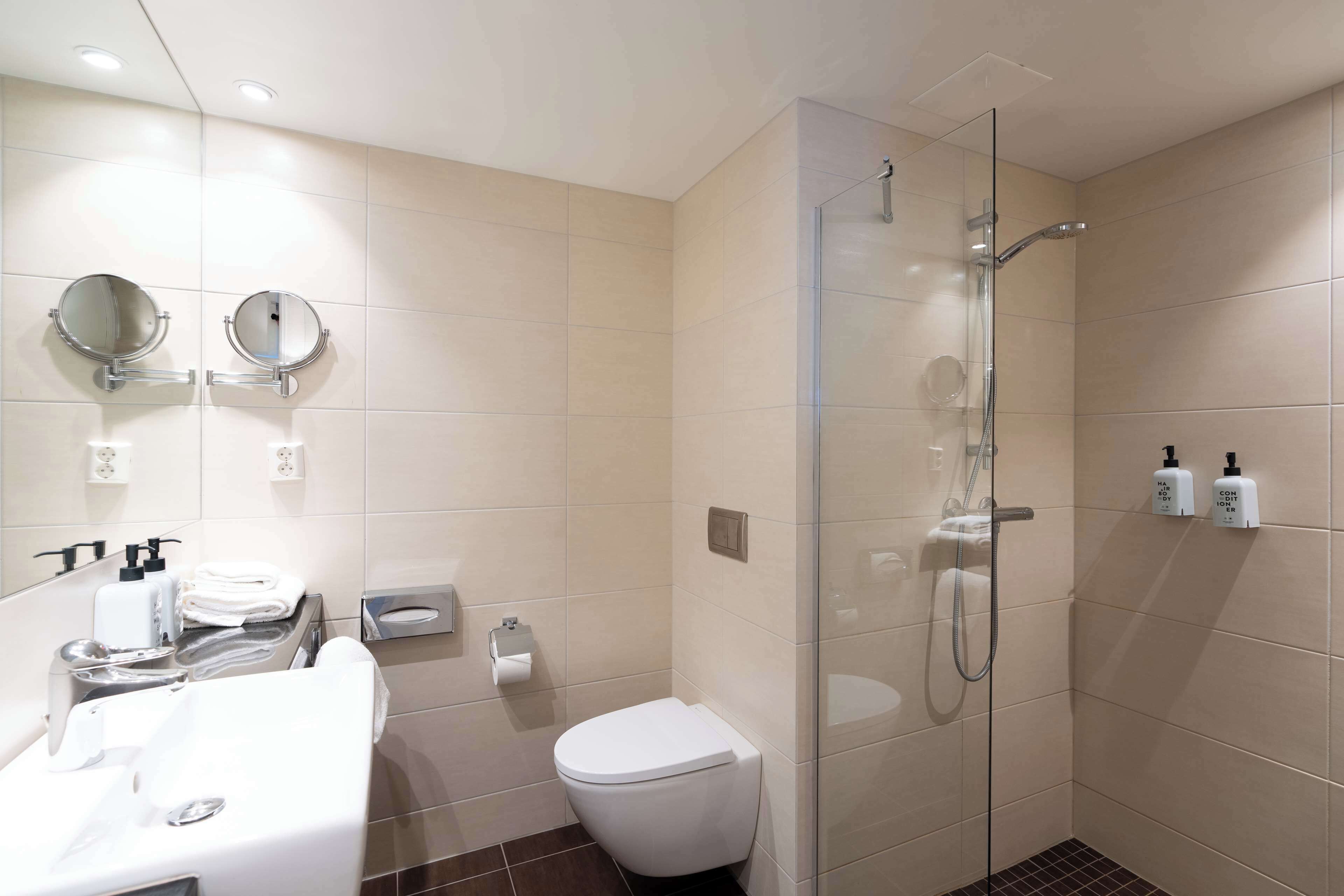 A modern bathroom with a glass-enclosed shower, a white sink with a mirror, and a toilet.