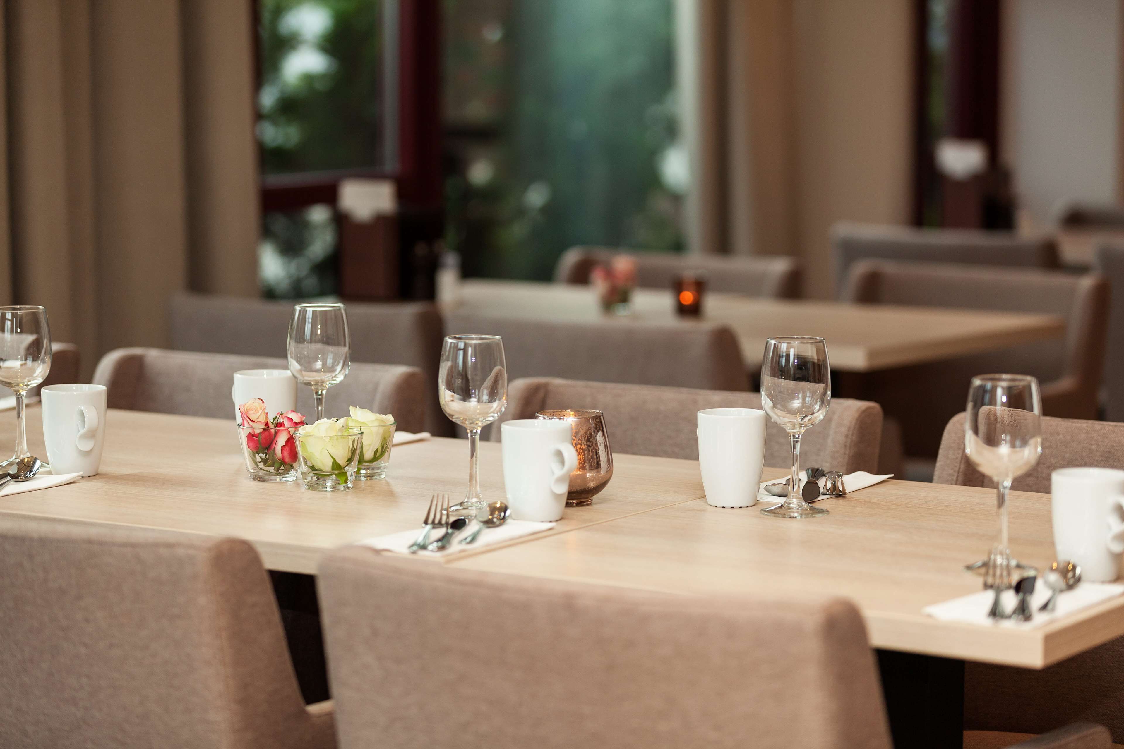 A restaurant with tables set for dining, featuring clear glassware, white cups, and a vase with flowers.