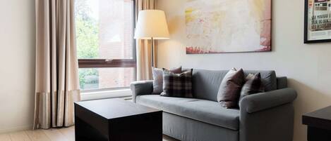 A modern living room with a grey sofa, a black coffee table, and a large window with curtains.