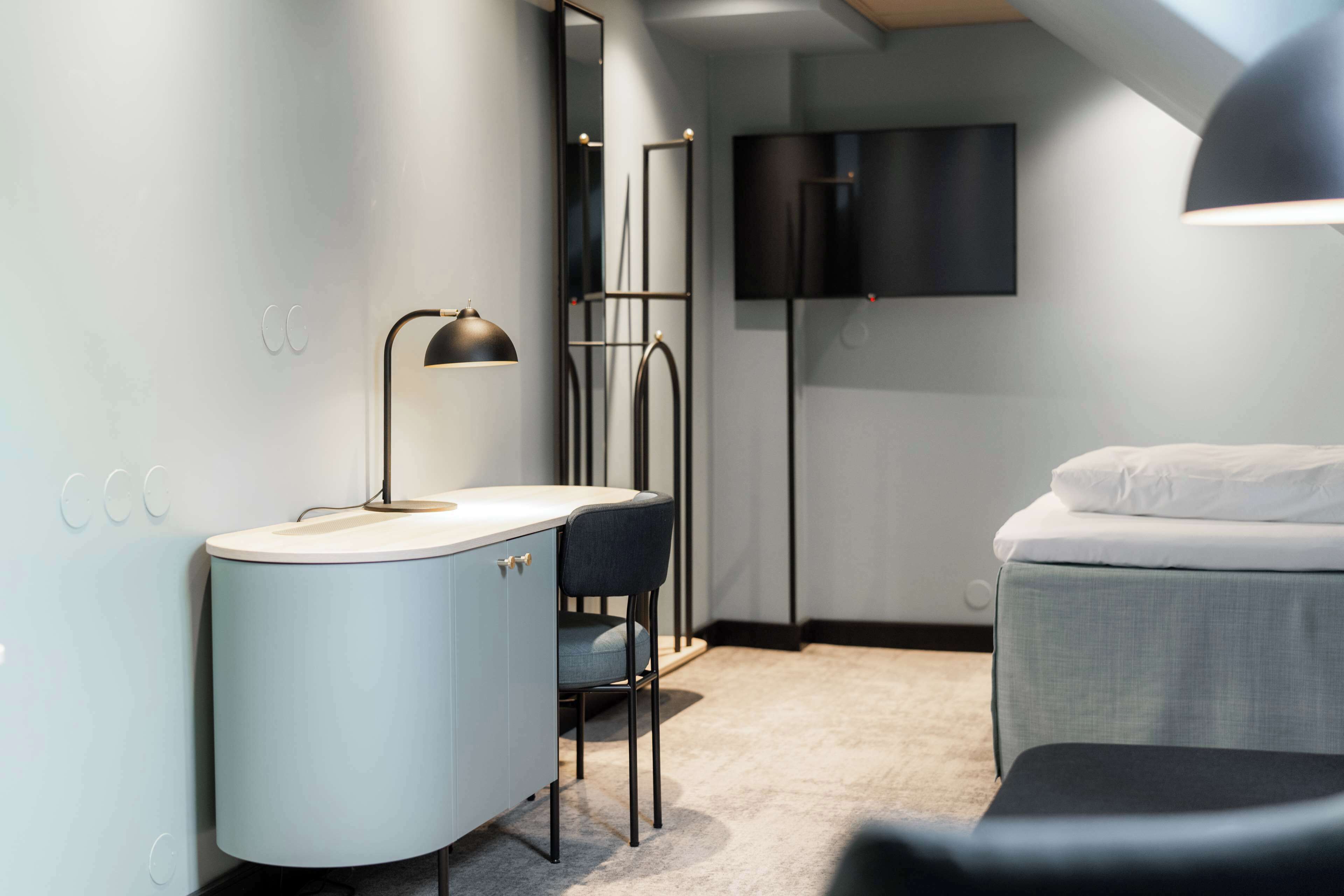 A modern bedroom with a bed, a desk, a chair, and a floor lamp.