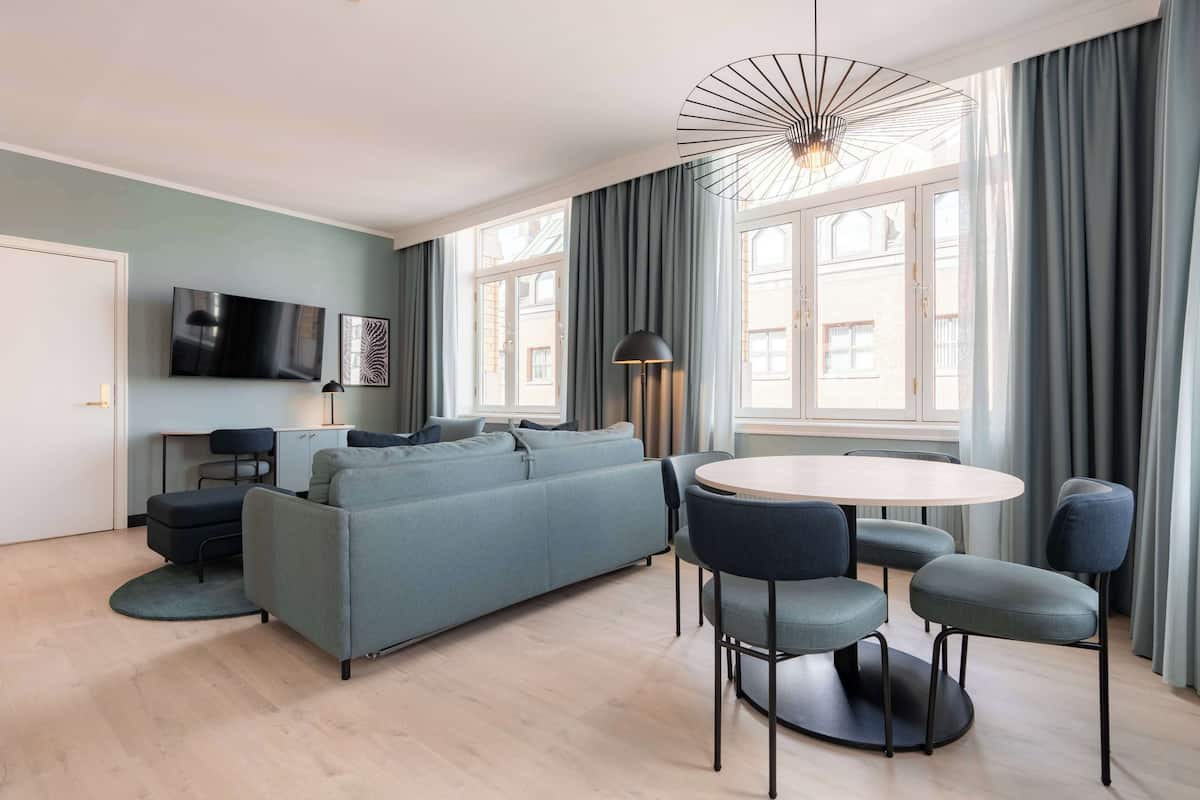 A modern living room with a sofa, chairs, a round table, a TV, and a large window with curtains.