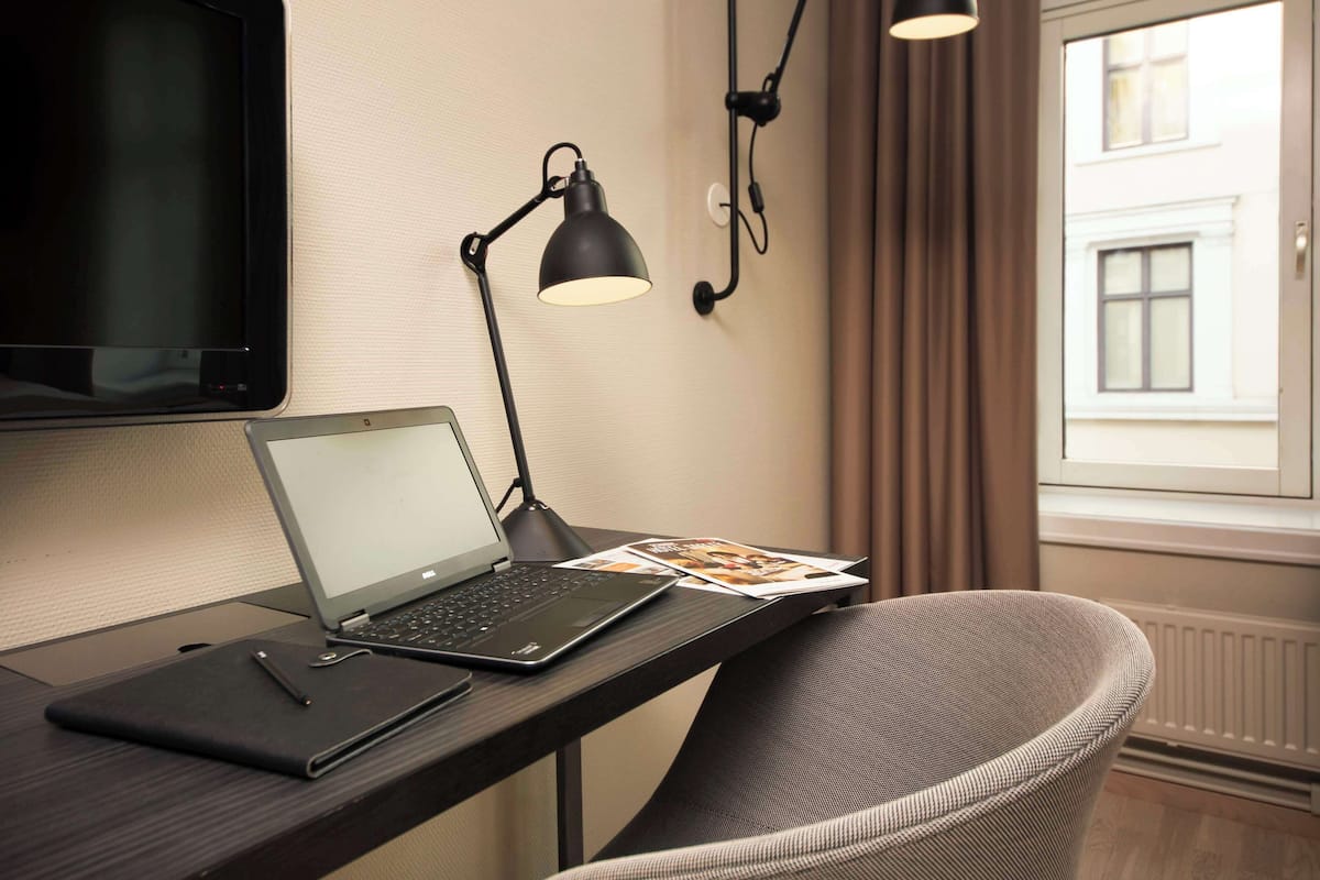 A laptop on a desk with a lamp, a chair, and a window with curtains.