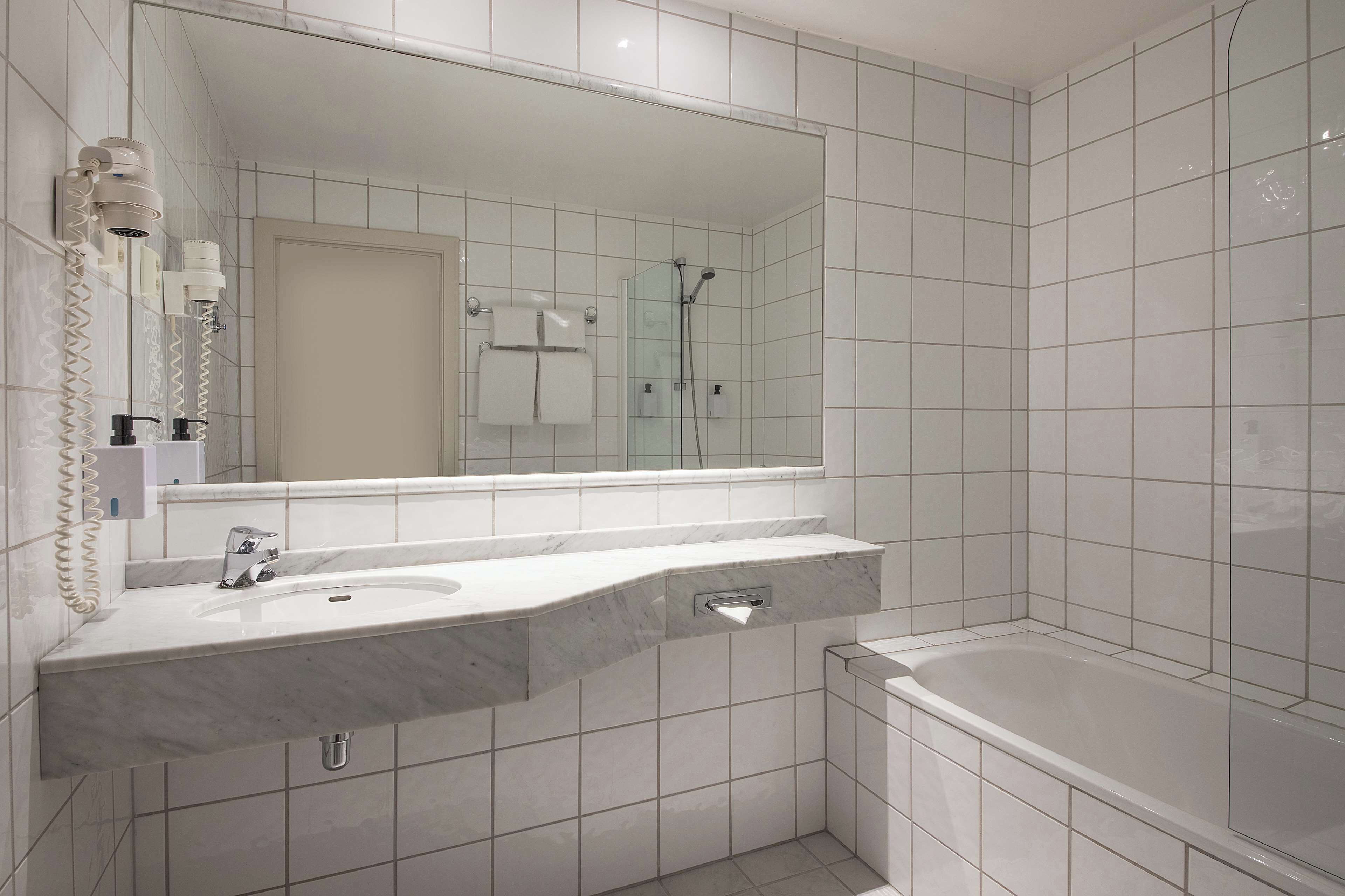 A modern bathroom with a large mirror, a sink with a marble countertop, a shower, and a bathtub.