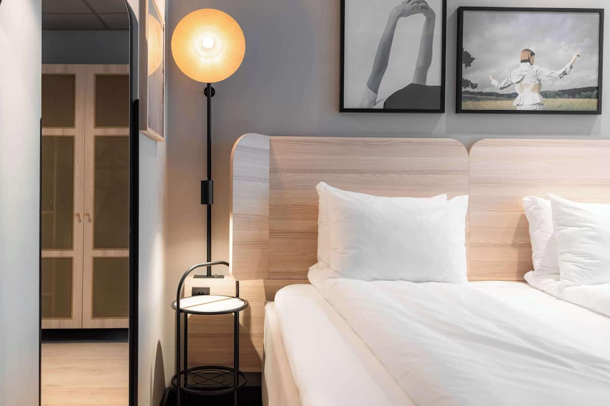 A neatly made bed with white bedding, a bedside table with a lamp, and two framed pictures on the wall.