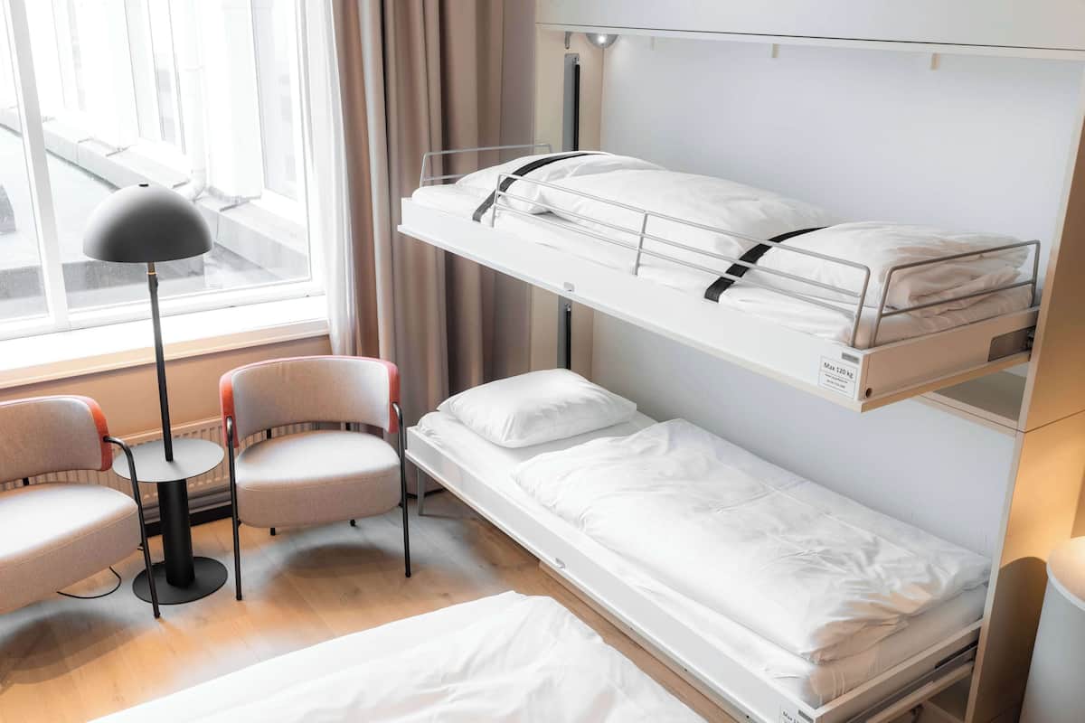 A bunk bed with a desk and chairs, a window with curtains, and a lamp.