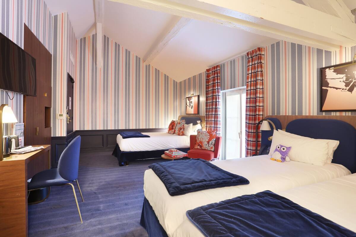A hotel room with two beds, a desk, a chair, and striped wallpaper.
