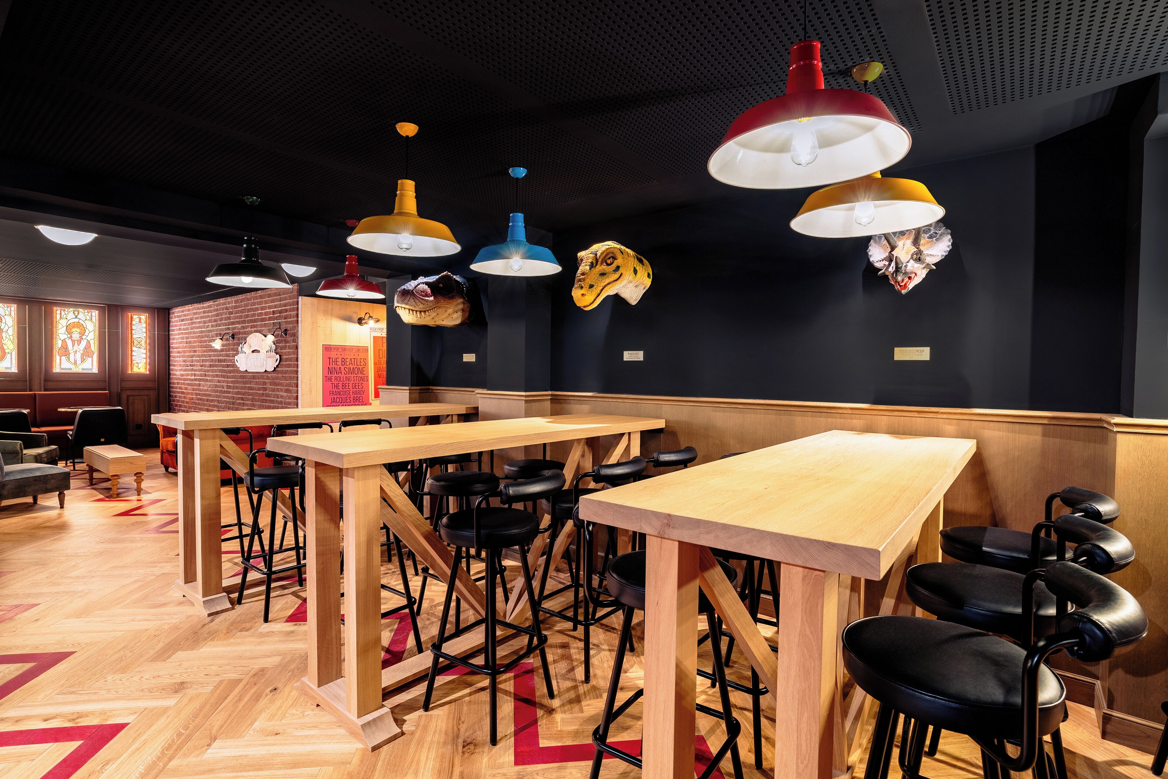 A restaurant interior with wooden tables and black stools, hanging pendant lights, and decorative animal heads on the wall.
