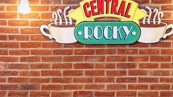A brick wall with a neon sign reading "CENTRAL ROCKY" and an orange tufted sofa.