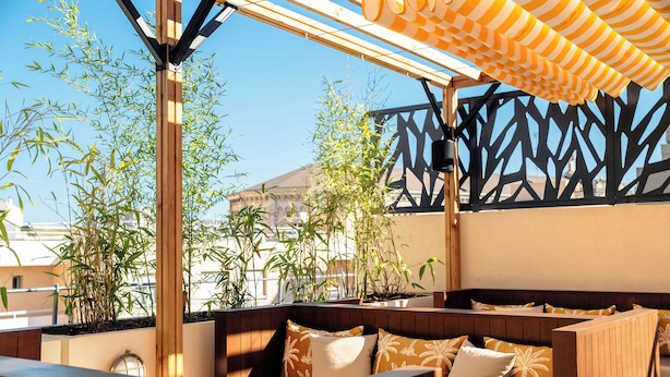 An outdoor seating area with wooden benches and cushions, surrounded by bamboo plants and a decorative metal fence. - RockyPop Marseille hôtel (Marseille)