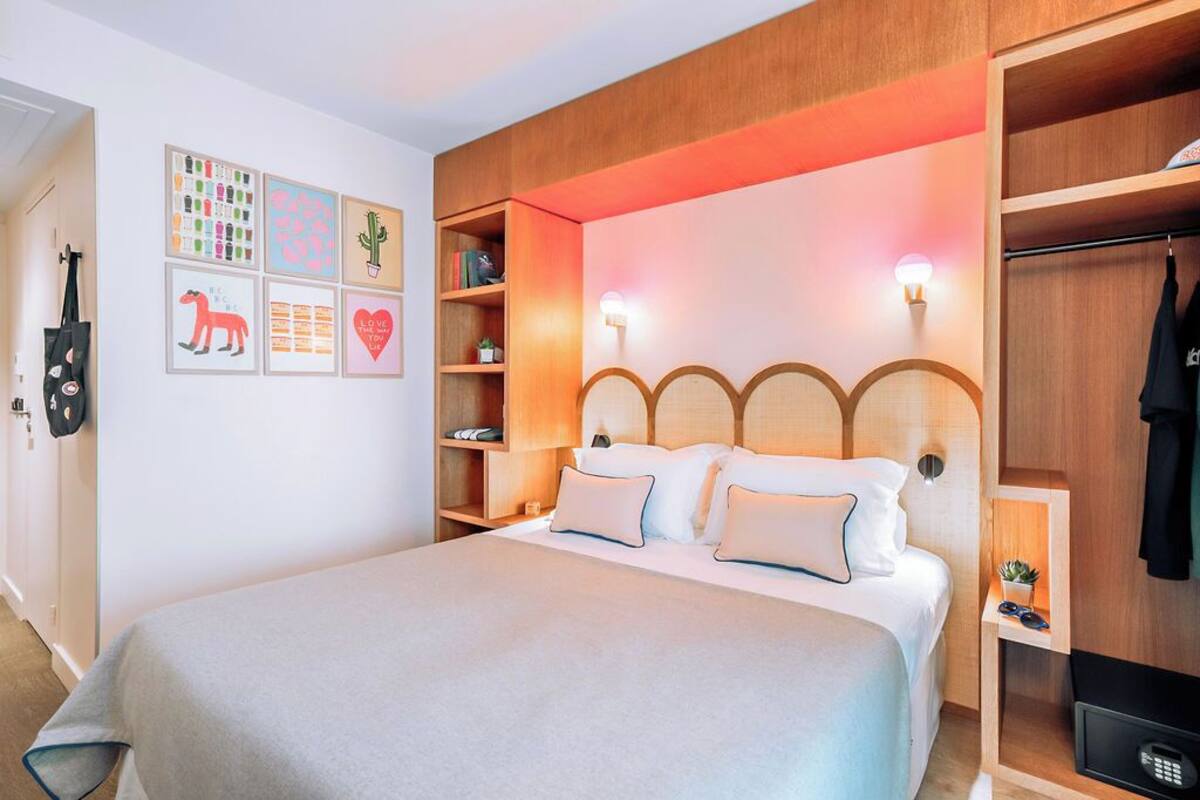 A neatly arranged hotel room with a bed, bedside tables, a wardrobe, and wall-mounted shelves.