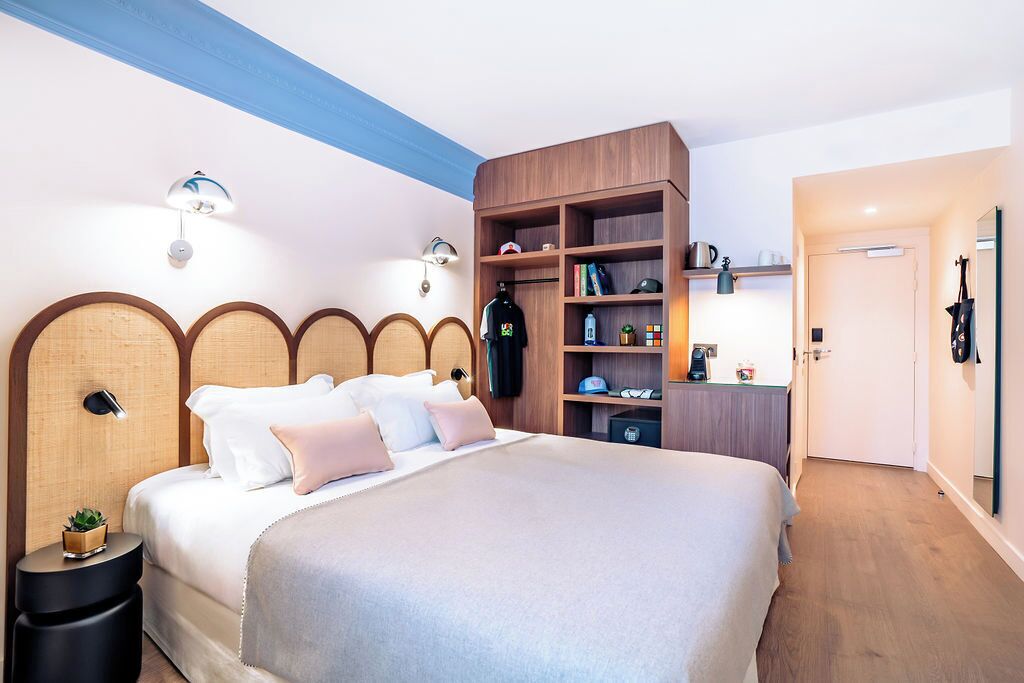A modern bedroom with a large bed, wooden headboard, bedside tables, a built-in bookshelf, and a small desk with a chair.