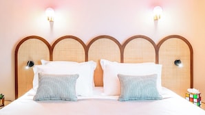 A neatly made bed with white linens and striped pillows, a wooden headboard with a woven texture, and wall-mounted light fixtures. - RockyPop Marseille hôtel (Marseille)