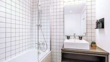 A modern bathroom with white tiled walls, a white bathtub, a wooden vanity with a sink, and a mirror.