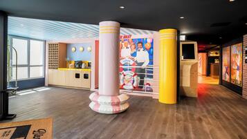 A hotel lobby with a reception desk, a large poster, and a wooden floor.