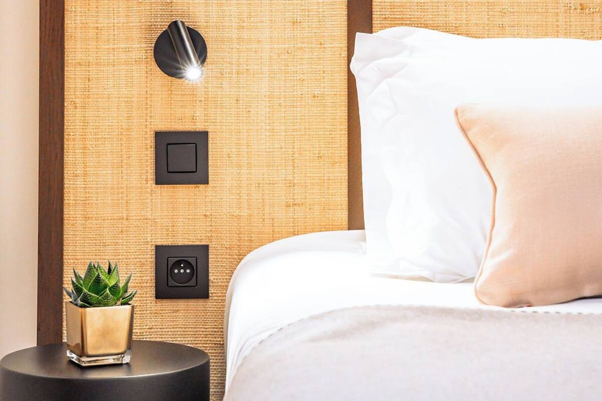 A bedroom with a bed, a nightstand, a wall-mounted light, and a small plant.